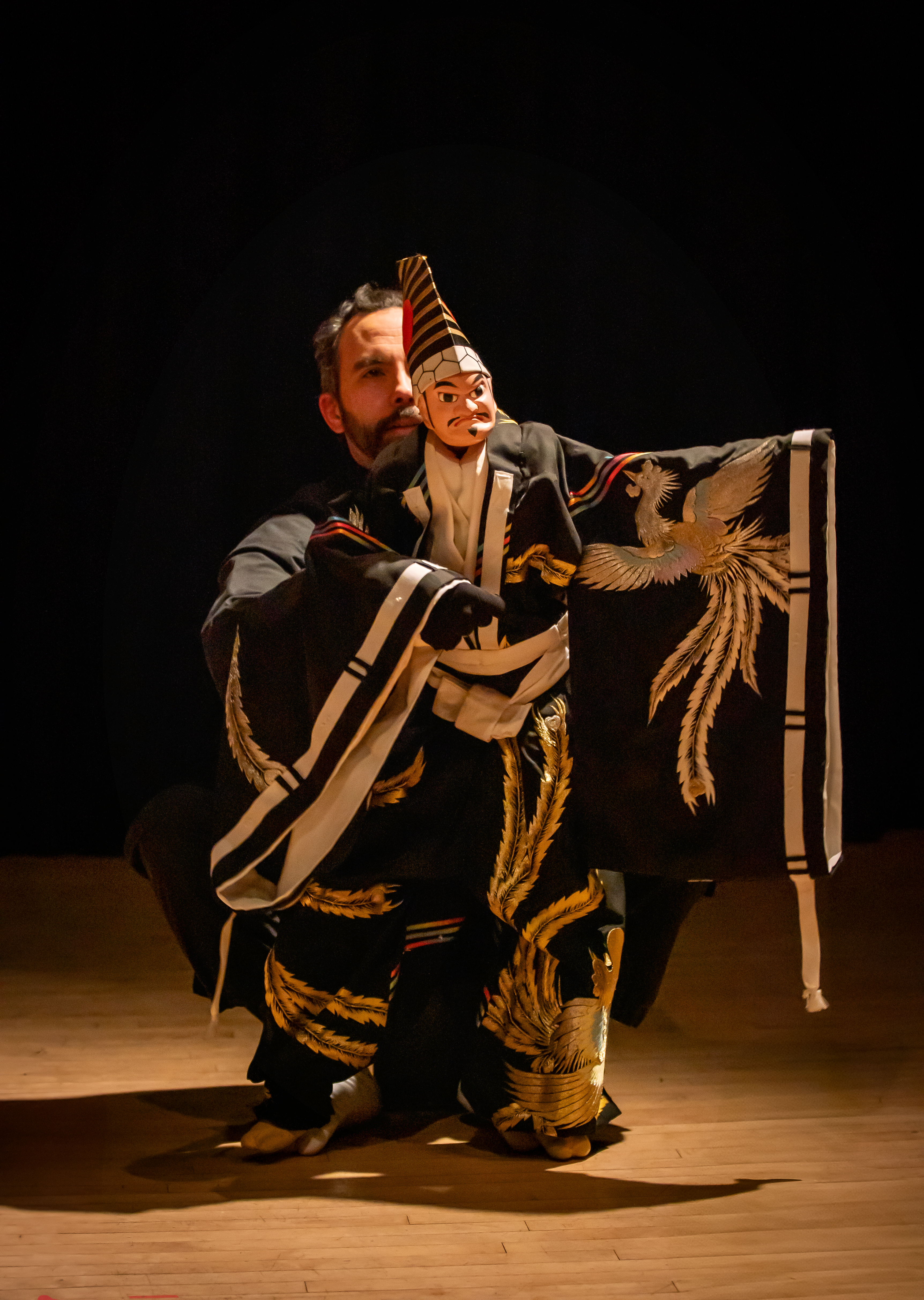 a biracial person with long black hair performs with a puppet of a human figure in long robes and a tall hat.