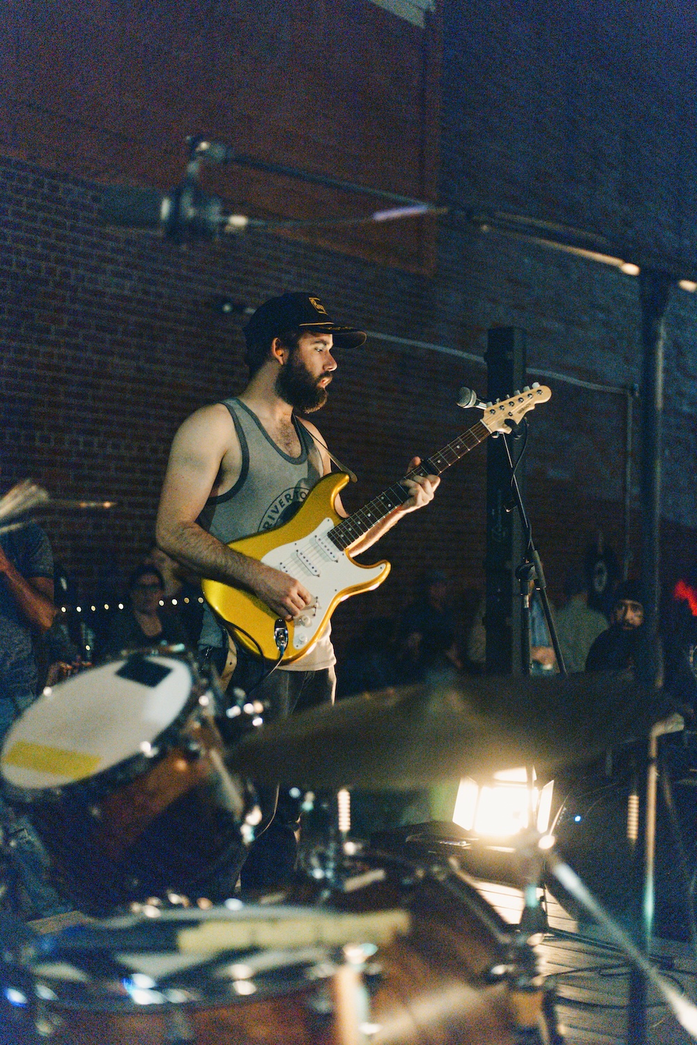A medium built white man with short, light-brown hair and a dark brown, medium length, full beard poses with a yellow electric guitar.