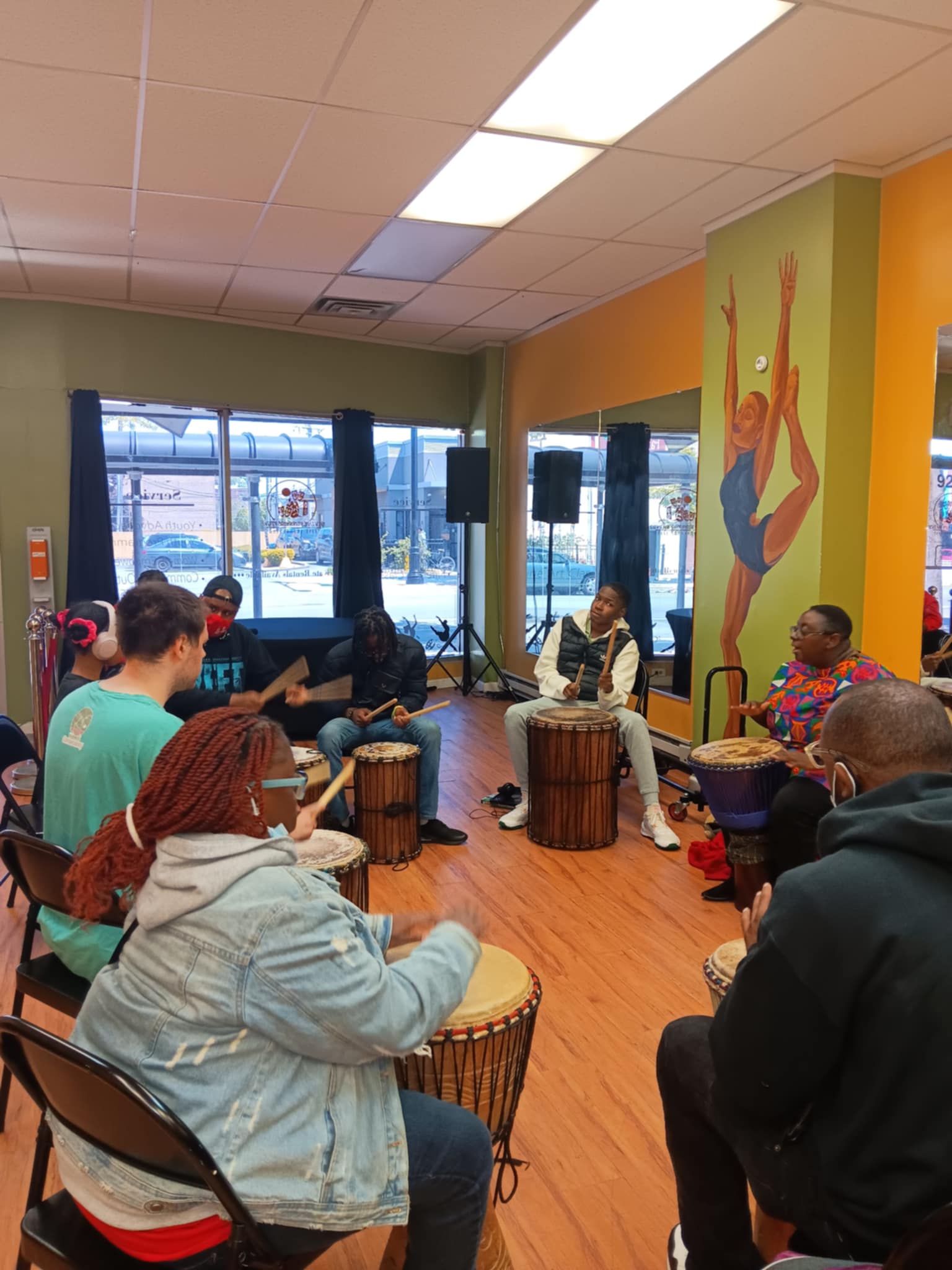 A Black autistic person with short dark hair leads a group in a drumming circle.