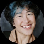 A headshot of a Taiwanese female-presenting artist with black hair, blue highlights and dark eyes. They are smiling at the camera.