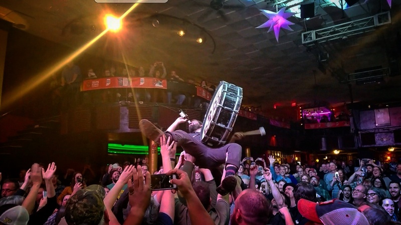  A man holding a drum crowd surfs indoors. 