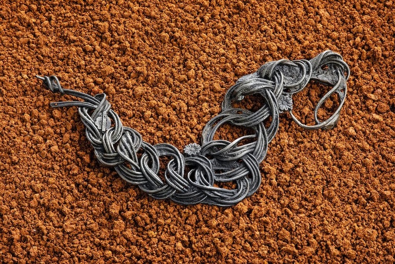  Image of a sculpture made with red clay soil. There is an iron cast jump rope laid on top of the soil. 