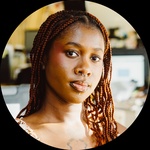 A headshot of a Black girl with tattoos. She has brown locks that go past her shoulders.