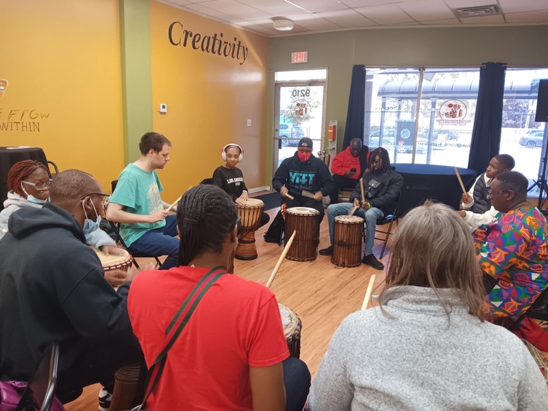  A Black autistic person with short dark hair leads a group in a drumming circle. 
