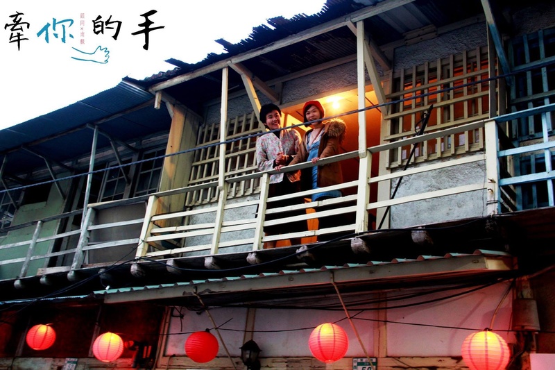  Two performers stand on a wooden balcony. Red lanterns hang below the building. 