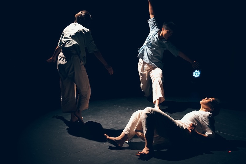  Three dancers perform on a dark stage. 