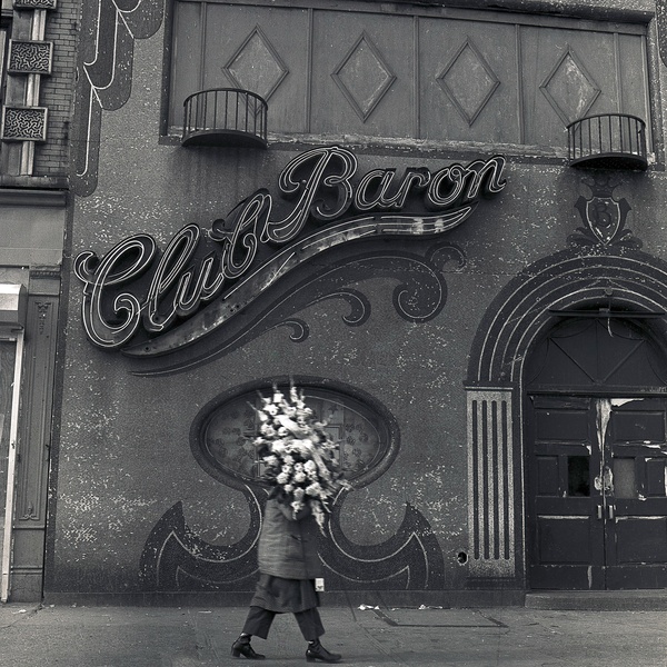  A black and white photograph of Club Baron with a figure in front holding a large bunch of flowers. 