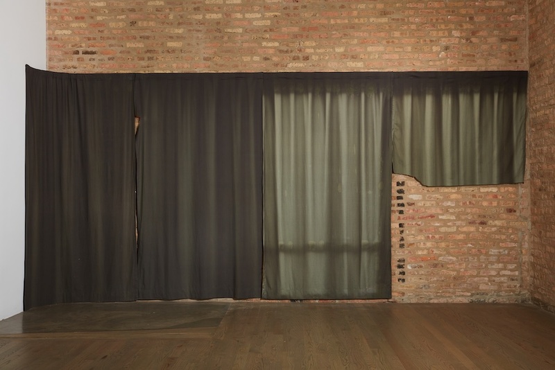  A small brick wall sits in front of a dark green curtain in sunlight. 