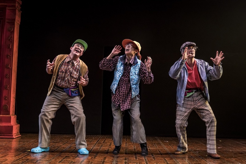  Three performers stand on stage. They are dressed in fun patterned button down shirts with loose khaki pants. All of them are posed humorously. 