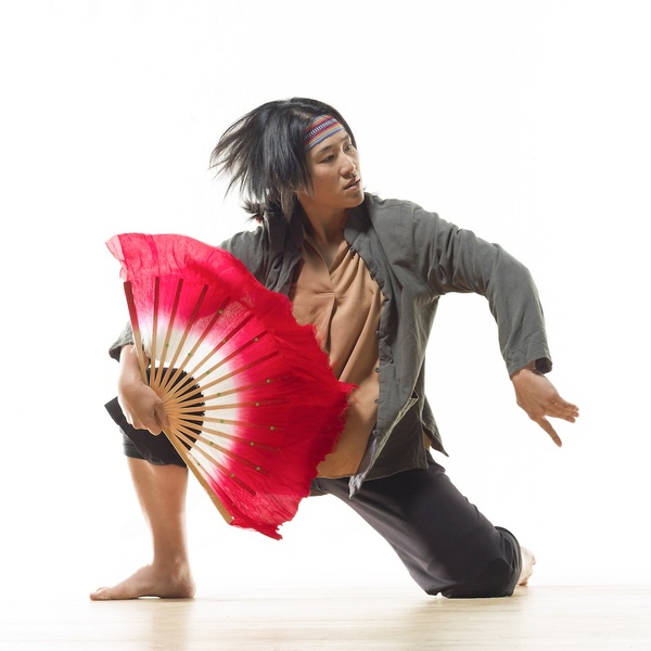  A Taiwanese female-presenting artist with black hair, dark eyes poses with a red fan. 