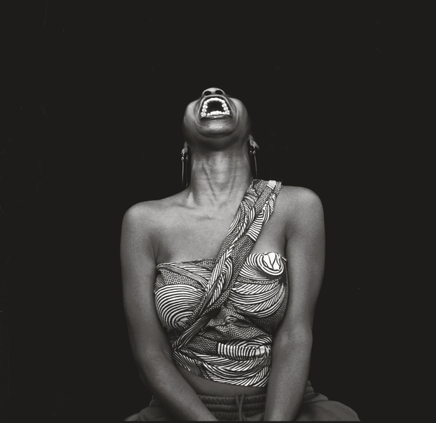  A black and white photograph of a Black woman shouting upwards. 