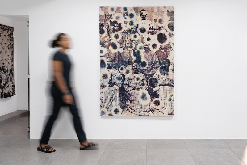  Installation shot of a print in a white all gallery. A figure is walking by in front of the print. 