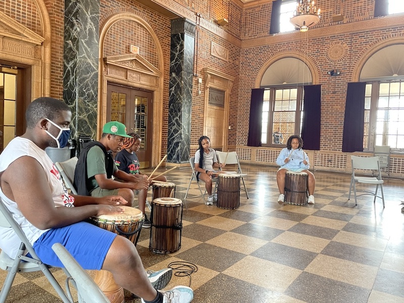  A Black autistic person with short dark hair leads a group in a drumming circle. 