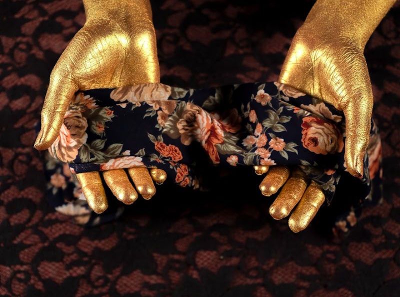  Two gold hands hold out a floral patterned fabric on a dark background. 
